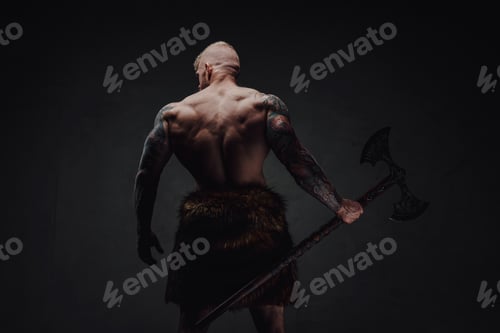Preview: Rear view of healthy tattoed warrior in fur with axe on a dark background