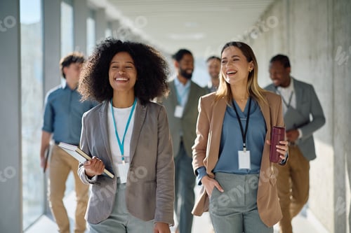 Preview: Young happy businesswomen and their colleagues walking through the hallway.