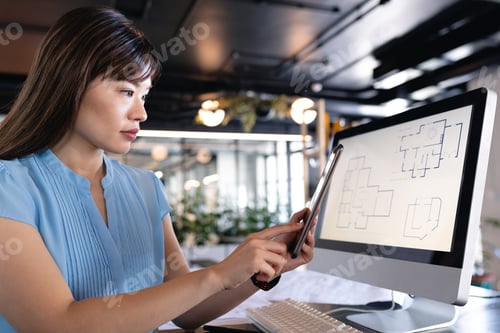 Preview: Asian woman working on computer and holding a digital tablet