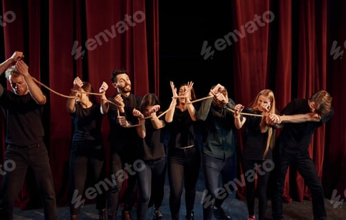 Preview: Knot in the hands. Group of actors in dark colored clothes on rehearsal in the theater
