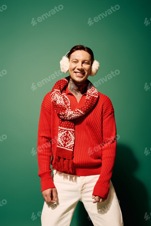 Preview: A cheerful young man in a red sweater and festive scarf enjoys winter with a playful smile indoors