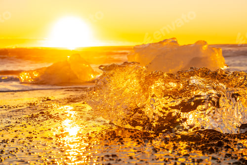 Preview: Clear ice at sunrise on Diamond Beach next to Jokulsarlon in winter in Iceland, with the sun