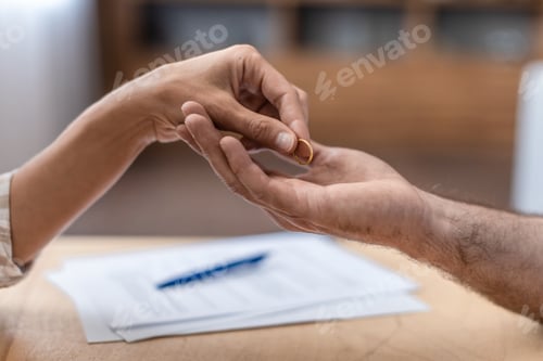 Preview: Hand of adult caucasian female gives ring to her ex husband at table with divorce papers, close up