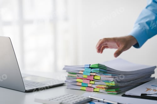 Preview: Businessman working on stacks of documents to search for information and check documents on office d