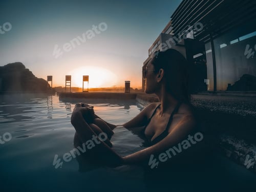 Preview: You g woman sitting in spa pool outside watching sunset golden hour with sunglasses in bathing suit