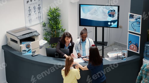 Preview: Secretary working at busy hospital reception desk to help patients