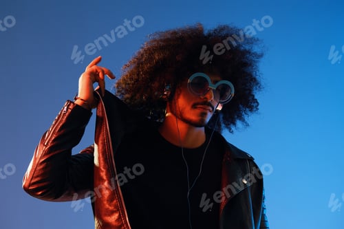 Preview: Portrait of a stylish man with curly hair with glasses and headphones on a blue background