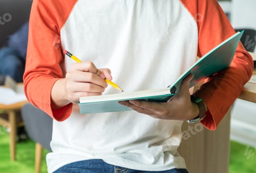 Preview: Close up at Young teenager boy writing on blue notebook