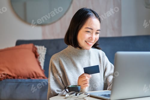 Preview: Portrait of korean woman shopping online, using her credit card and laptop to order delivery from