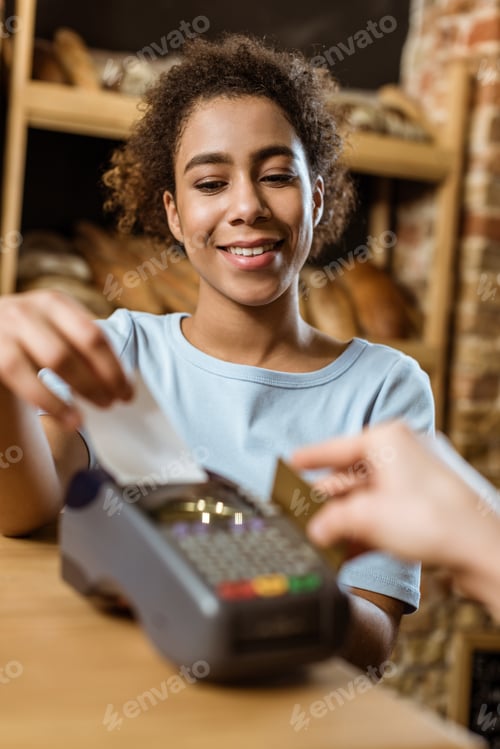 Preview: close-up shot of happy cashier with pos terminal receiving purchase from client at pastry store