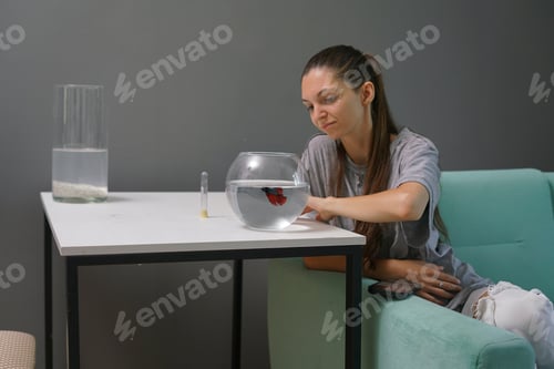 Preview: The woman watches the surface of the water while observing her colorful fish in a bowl, enjoying a r