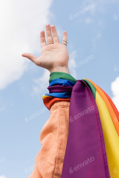 Preview: Cropped view of gay man with lgbt flag on hand and sky at background outdoors, International day