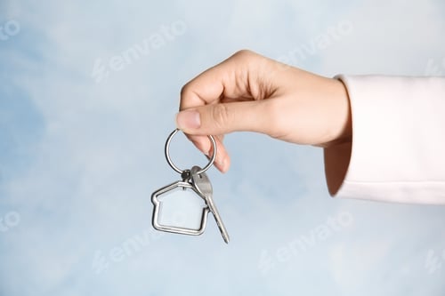 Preview: Woman holding house key with trinket on color background, closeup