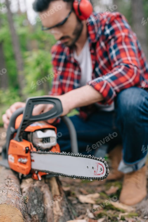 Preview: selective focus of lumberjack repairing electric chainsaw in forest
