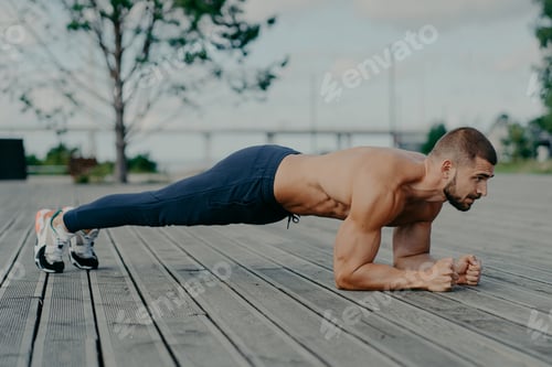 Preview: Motivated male athlete does abs exercise, enjoys bodybuilding training outdoor and stands in plank