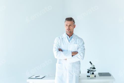 Preview: handsome scientist standing with crossed arms near table isolated on white