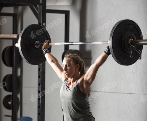 Preview: Close up of strong young woman lifting barbell over her head in gym.
