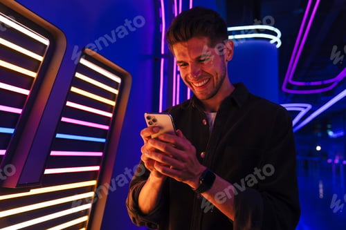 Preview: Young bristle man wearing black shirt smiling while using mobile phone