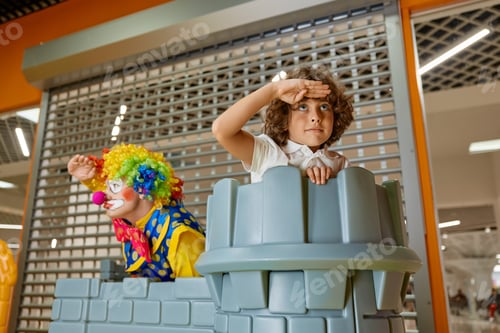 Preview: Excited clown playing game with cheerful boy at indoor amusement park