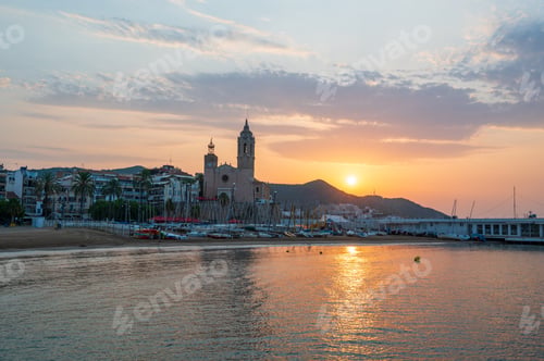 Preview: Sunrise illuminating sitges church and beach with boats on shore