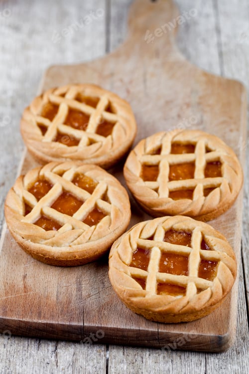 Preview: Fresh baked tarts with marmalade or apricot jam filling on cutting board on on rustic wooden table.