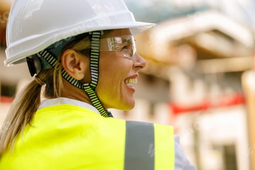 Preview: Smiling female construction worker in protective helmet standing against on construction background