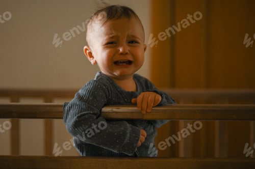 Preview: A crying baby is standing in a crib. A boy at home in the bedroom is crying
