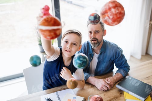Preview: Mature father with small son sitting at table indoors, working on school project