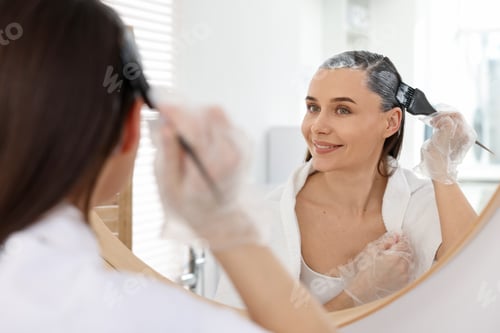 Preview: Beautiful woman dyeing her hair near mirror at home