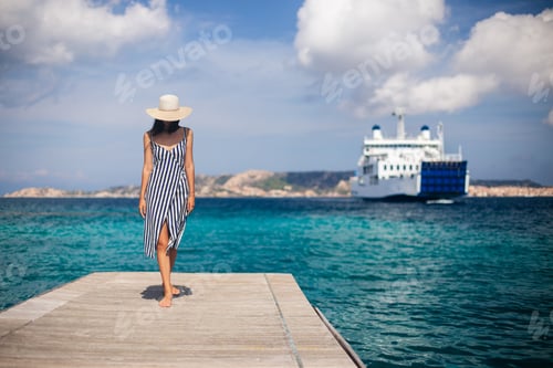 Preview: Beautiful young woman in hat walking on wooden pier on Sardinia beach