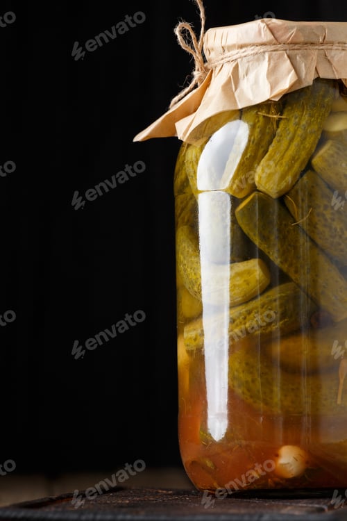 Preview: Pickled cucumbers in a jar on a dark background close-up.