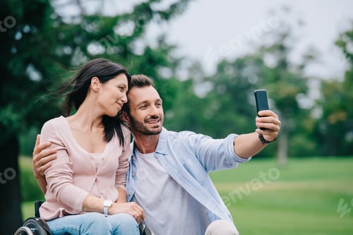 Preview: happy man taking selfie with disabled girlfriend on smartphone in park