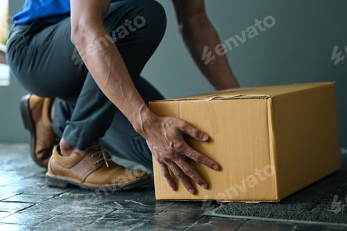 Preview: Cropped image of male courier putting parcel cardboard box near entrance.
