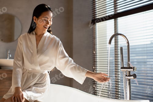 Preview: Positive attractive asian lady sitting on bath in modern bathroom