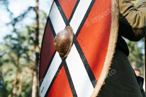 Preview: Antique round red shield on the back of a viking outdoors, close-up, side view