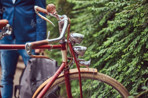 Preview: Male dressed in casual clothes, standing near a retro bicycle in a park.
