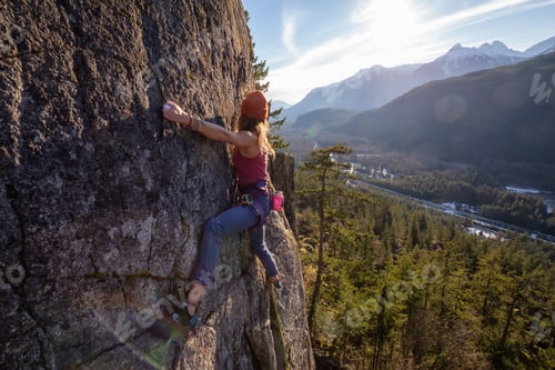 Preview: Female Rock climber climbing on the edge of the cliff during a sunny winter sunset