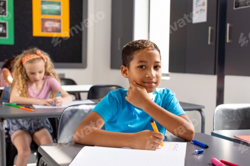Preview: In school, young biracial male student sitting at a desk in a classroom, looking thoughtful