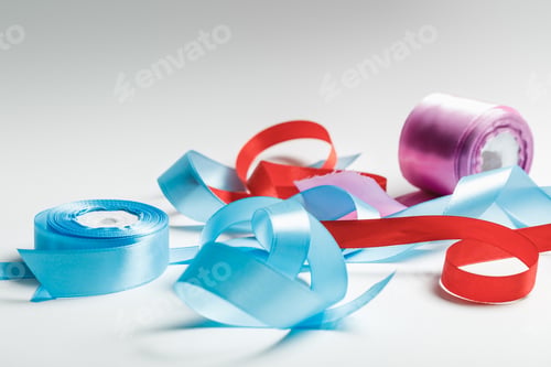 Preview: curved blue, red and purple satin ribbons with spools on grey background