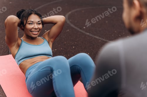Preview: Portrait of beautiful, smiling African American woman doing exercises, lying on yoga mat outdoors
