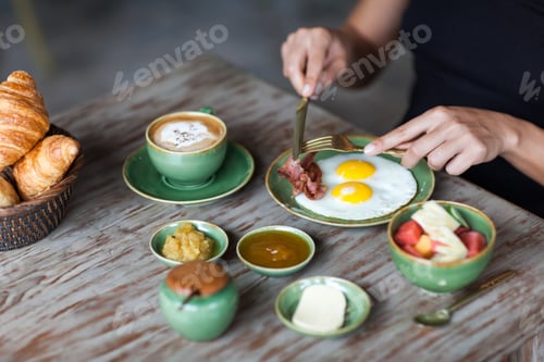 Visualização: Mulher cortando ovos fritos com garfo dourado e faca no café da manhã