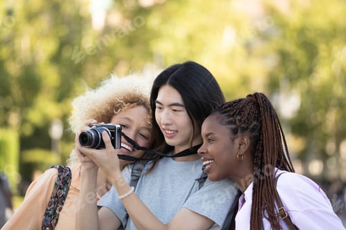 Preview: Smiling multi ethnic group of tourist friends checking the photos they have taken during their trip