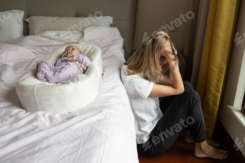 Preview: Tired Mother Suffering from experiencing postnatal depression. Newborn baby lying in cocoon on bed.