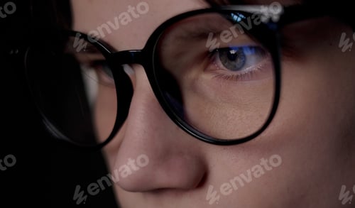 Preview: macro side view of focused man wears glasses is looking at light from the dark. Male uses pc scre