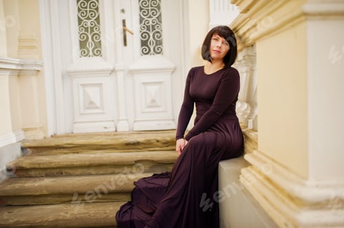 Preview: Adult brunette woman at violet gown background old vintage house with stairs.