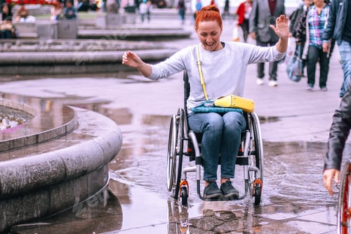 Preview: A girl in a wheelchair is having fun riding in puddles. An active cheerful woman with special needs