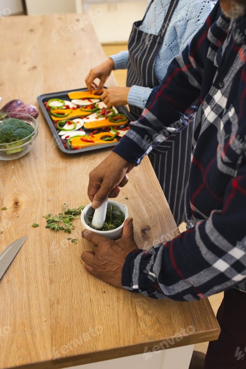 Preview: Midsection of diverse senior couple preparing healthy meal with vegetables in kitchen