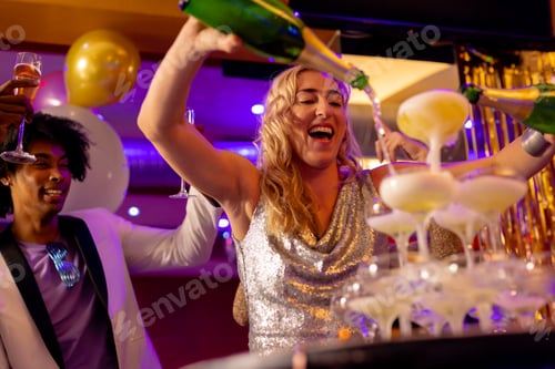 Preview: Happy caucasian woman pouring a champagne fountain into glasses with diverse friends at a nightclub