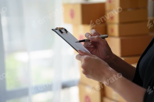Preview: Close-up of a young woman who owner an online business packing and checking balance against a laptop