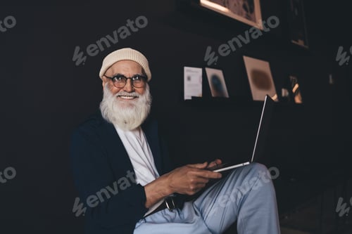 Preview: Cheerful senior man sitting on chair with laptop